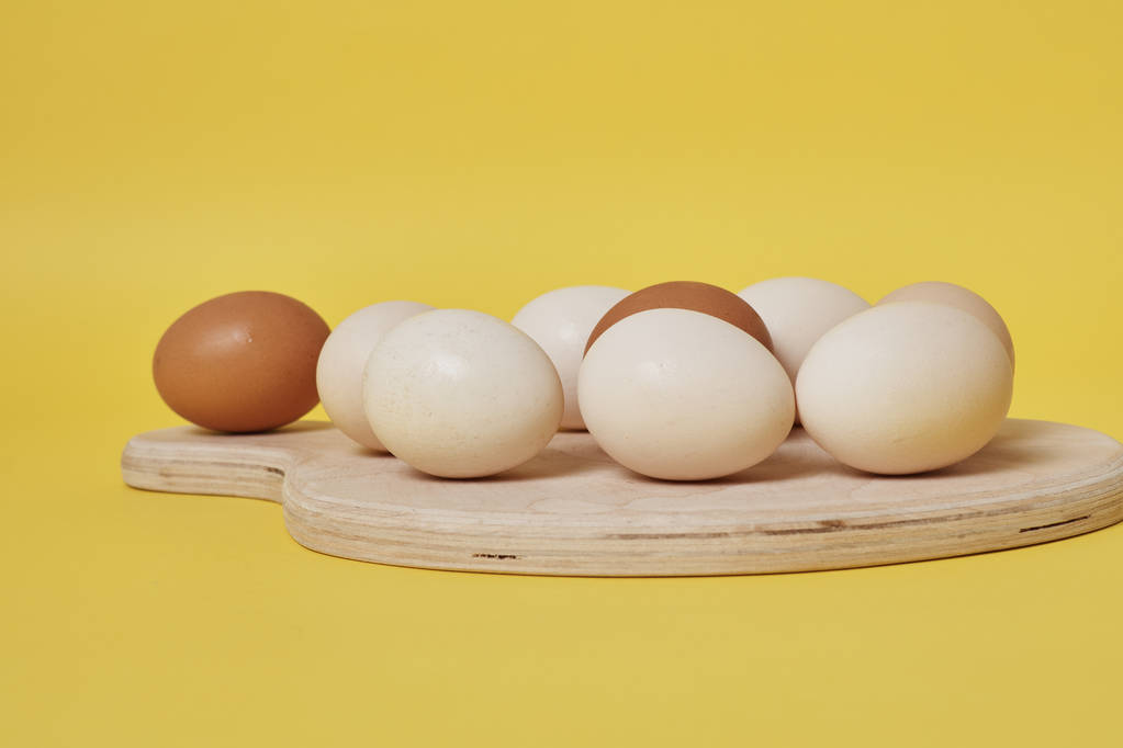 jaja na drewnianej desce na jasnożółtym tle - Zdjęcie, obraz