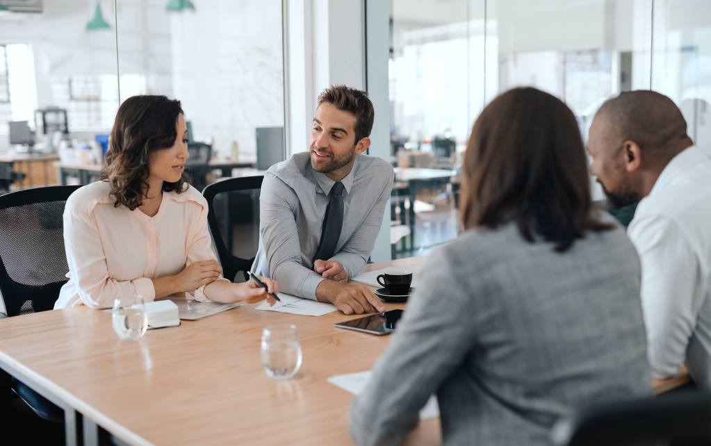 Grupo sorridente de empresários diversos sentados juntos em torno de uma mesa em uma sala de reuniões de escritório discutindo o trabalho
 - Foto, Imagem