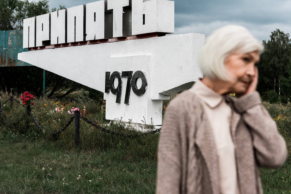 PRIPYAT, UKRAINE AUGUST 15, 2019: eläkkeellä oleva nainen seisoo muistomerkin lähellä pripyat-kirjaimin
 - Valokuva, kuva