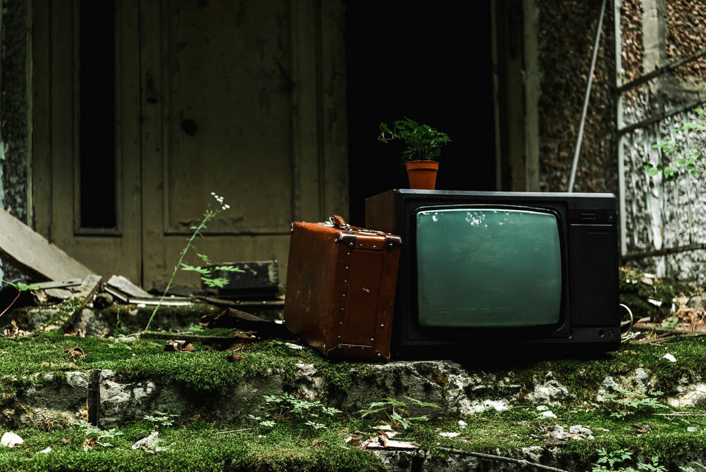 Retro-Fernseher in der Nähe von Vintage-Koffer auf grünen Treppen mit Schimmel  - Foto, Bild