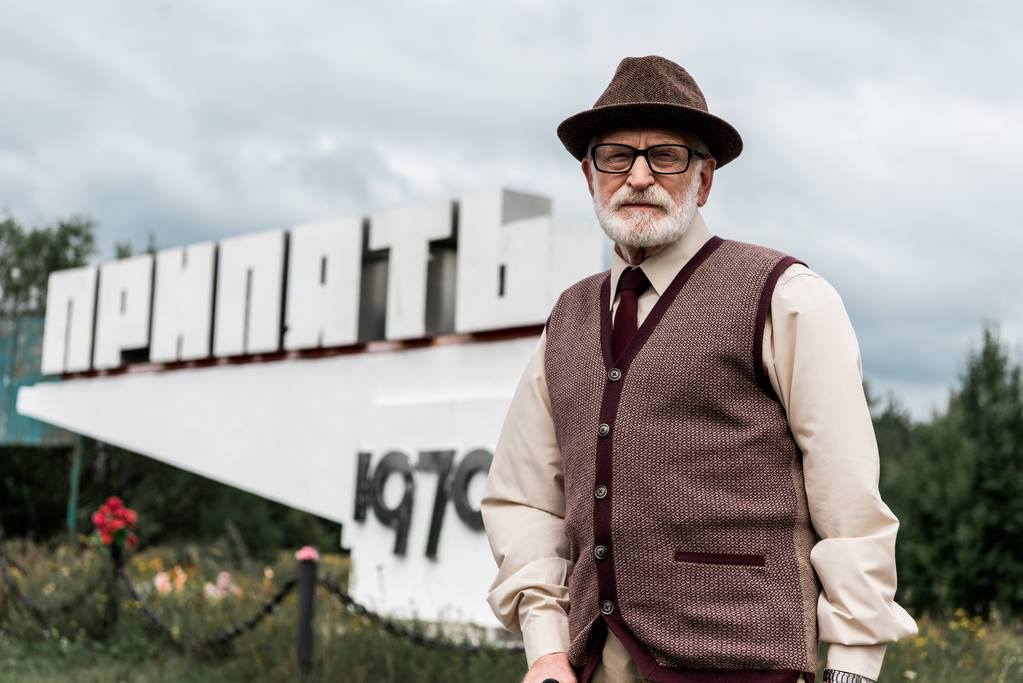 PRIPYAT, UCRAINA - 15 AGOSTO 2019: uomo anziano con gli occhiali in piedi vicino al monumento con lettere di pripiato
 - Foto, immagini