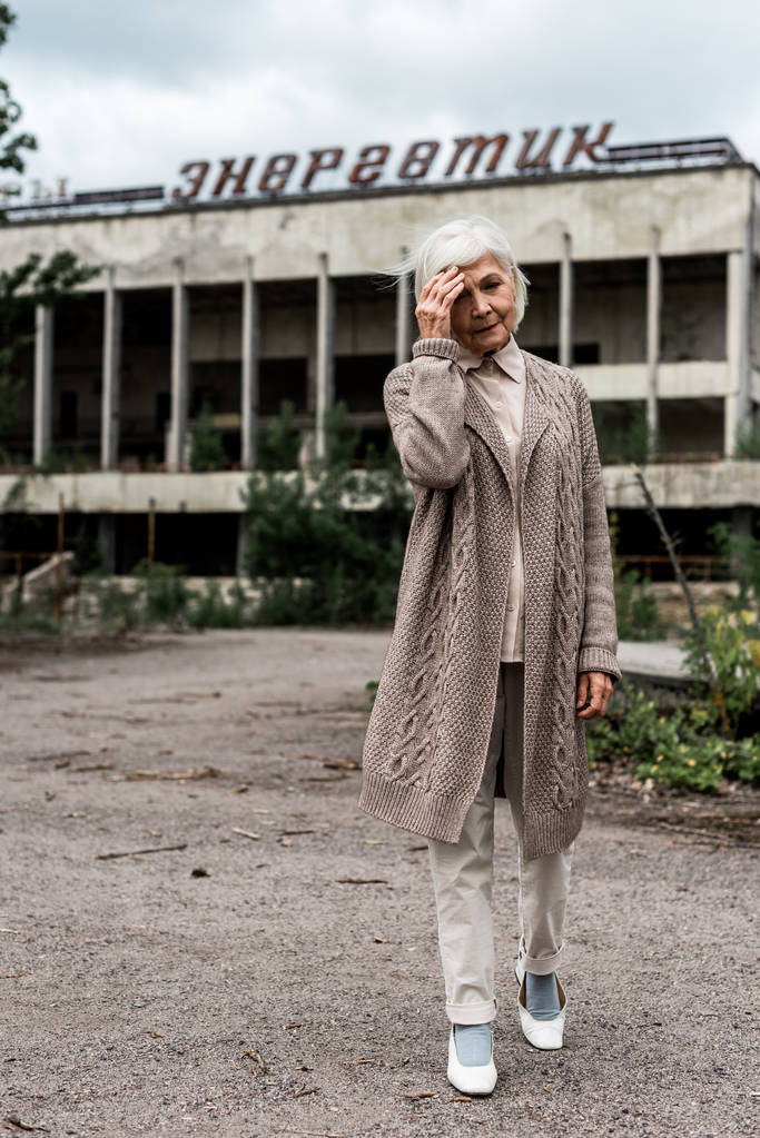pripjat, Ukraine - 15. August 2019: Seniorin läuft in Tschernobyl in der Nähe eines Gebäudes mit energiegeladenen Schriftzügen  - Foto, Bild