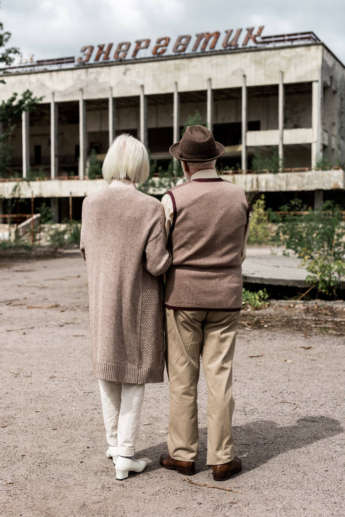 PRIPYAT, UCRANIA - 15 de agosto de 2019: vista trasera de una pareja jubilada parada cerca del edificio con letras enérgicas en chernobyl
  - Foto, imagen