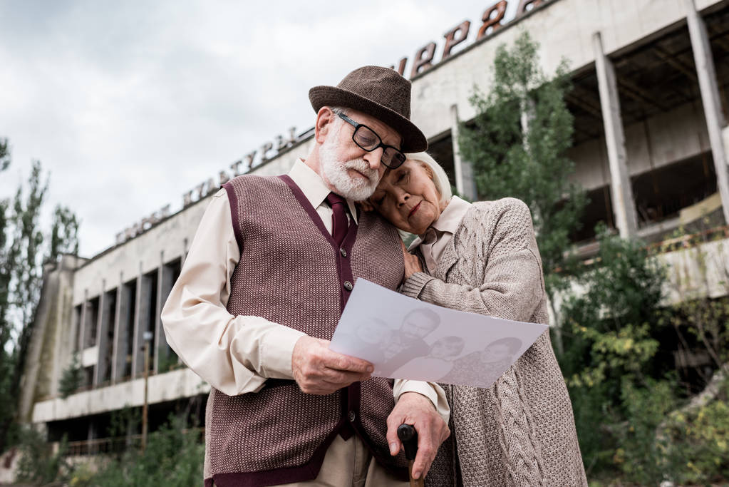 PRIPYAT, UKRAINE - 15 AOÛT 2019 : vue en angle bas d'un couple de personnes âgées regardant une photo près d'un immeuble à Tchernobyl
  - Photo, image