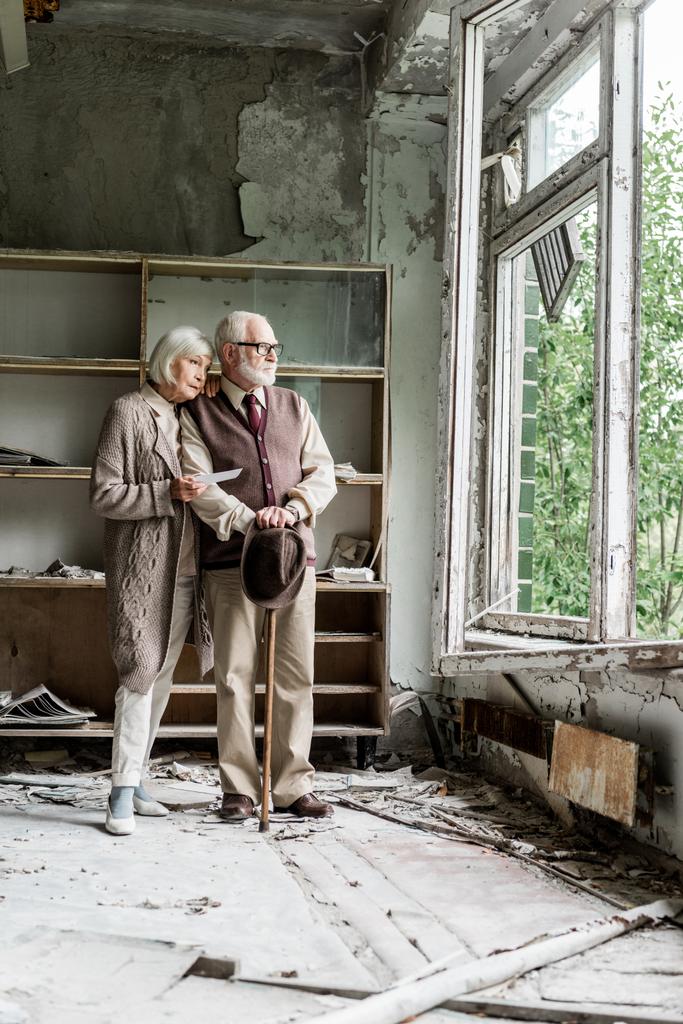 retired couple looking at window while standing in damaged classroom  - Photo, Image