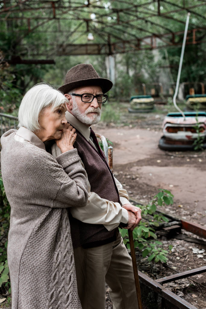 PRIPYAT, UCRANIA - 15 de agosto de 2019: triste anciana de pie con su esposo jubilado con sombrero
  - Foto, imagen