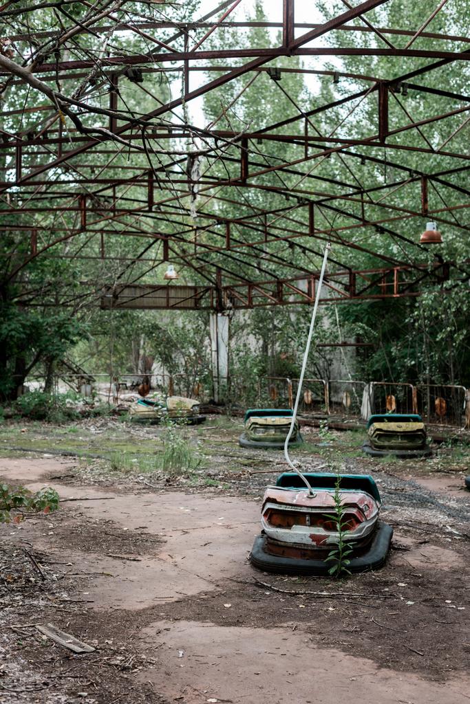 PRIPYAT, UCRANIA - 15 de agosto de 2019: coches de choque en el parque de atracciones abandonado cerca de los árboles
 - Foto, imagen