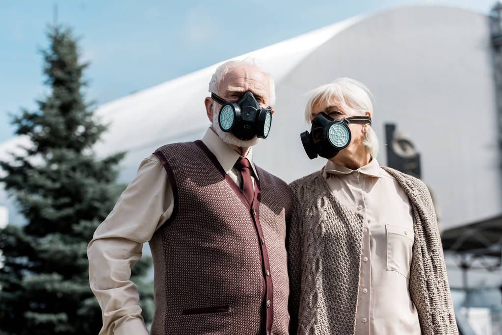 PRIPYAT, UKRAINE - AUGUST 15, 2019: retired couple in protective masks standing near abandoned chernobyl reactor  - Photo, Image