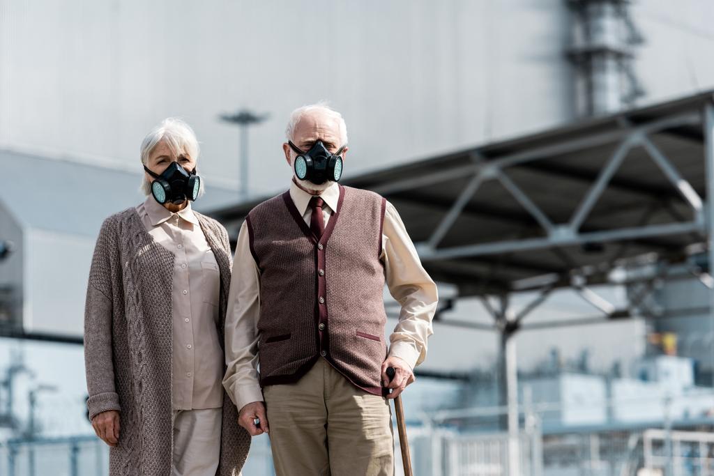 Прип'ять, Україна-15 серпня 2019: старша жінка і людина в захисних масках стояли біля покинутих чорнобильських реакторів  - Фото, зображення