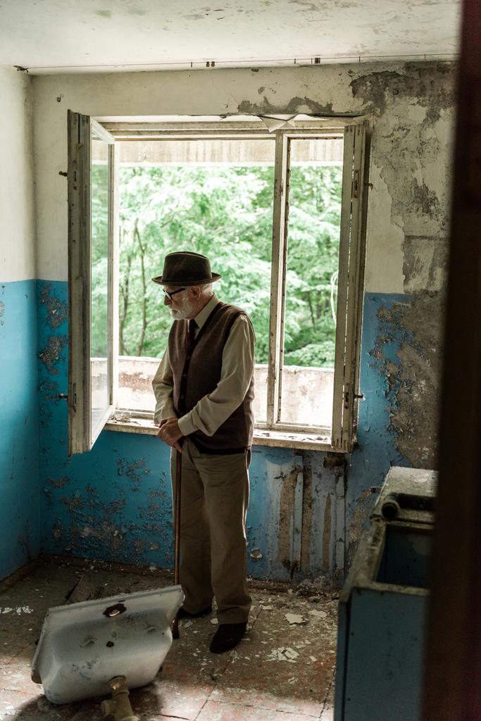 smutny starszy człowiek stojący z chodzeniem trzciny w uszkodzonym pomieszczeniu  - Zdjęcie, obraz