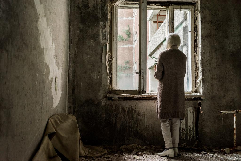 πίσω όψη των συνταξιούχων γυναίκα που κατέχουν φυτό σε άδειο δωμάτιο κοντά στα παράθυρα  - Φωτογραφία, εικόνα