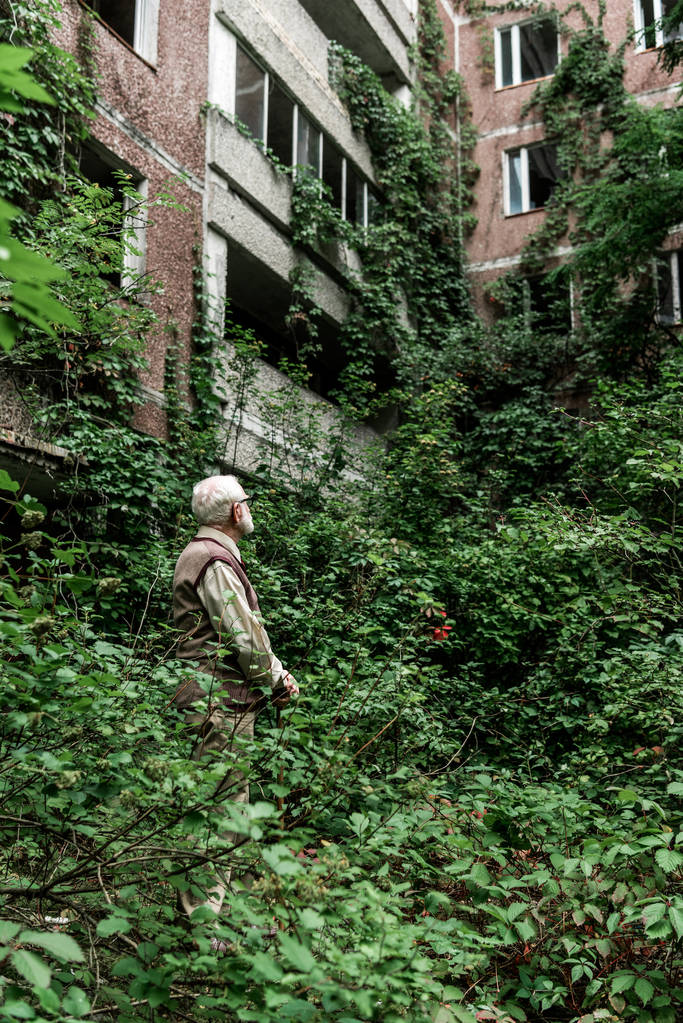 homme à la retraite dans des lunettes regardant maison envahie de feuilles
 - Photo, image