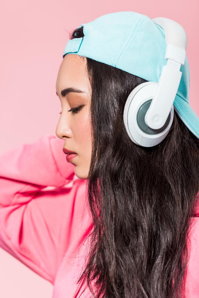 attrayant asiatique femme dans pullover et cap écoute musique isolé sur rose
  - Photo, image