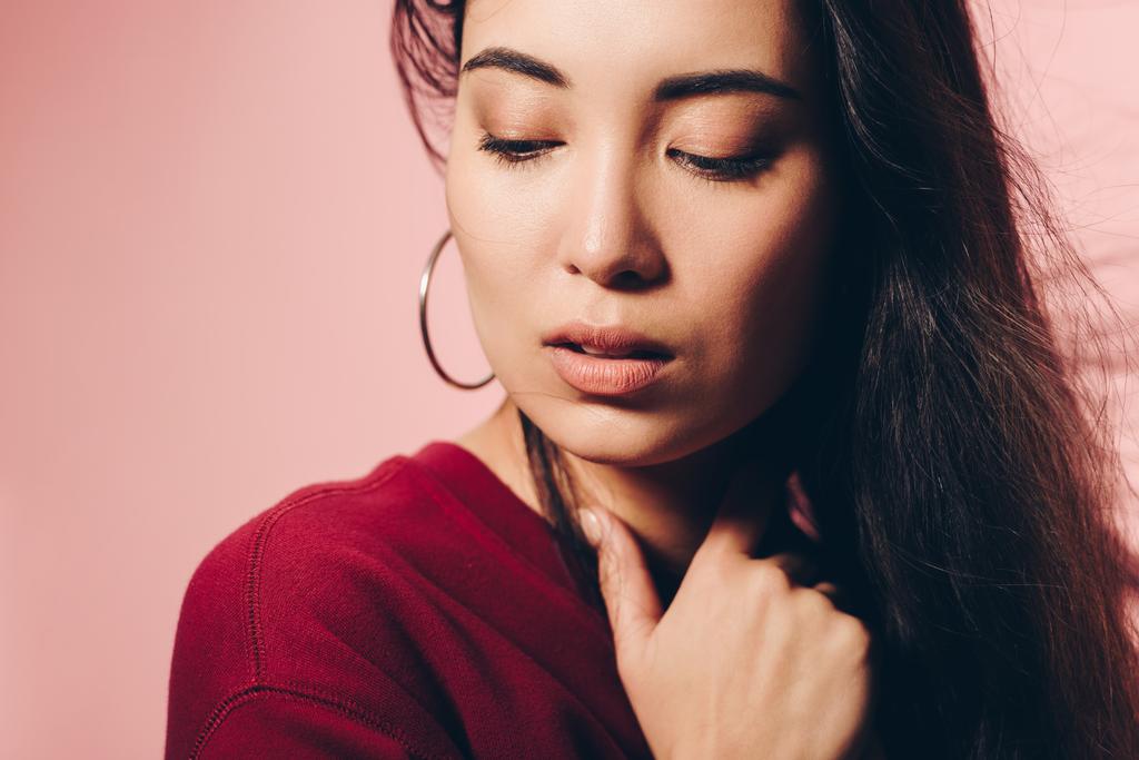 attractive asian woman in red sweater looking down isolated on pink  - Photo, Image