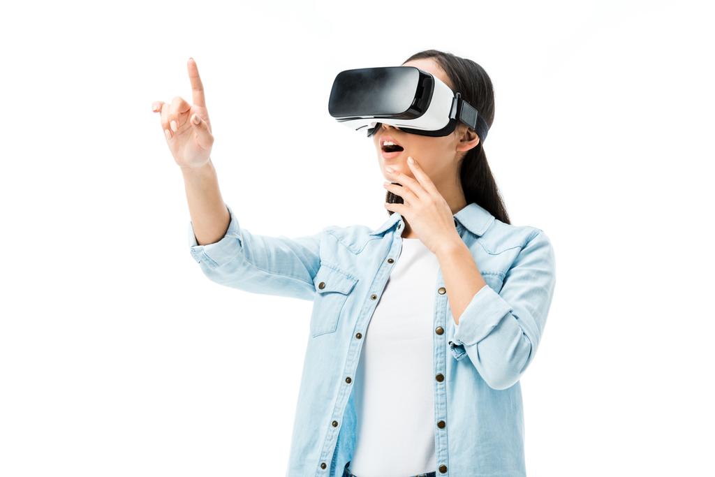 shocked woman in denim shirt with virtual reality headset pointing with finger isolated on white  - Photo, Image