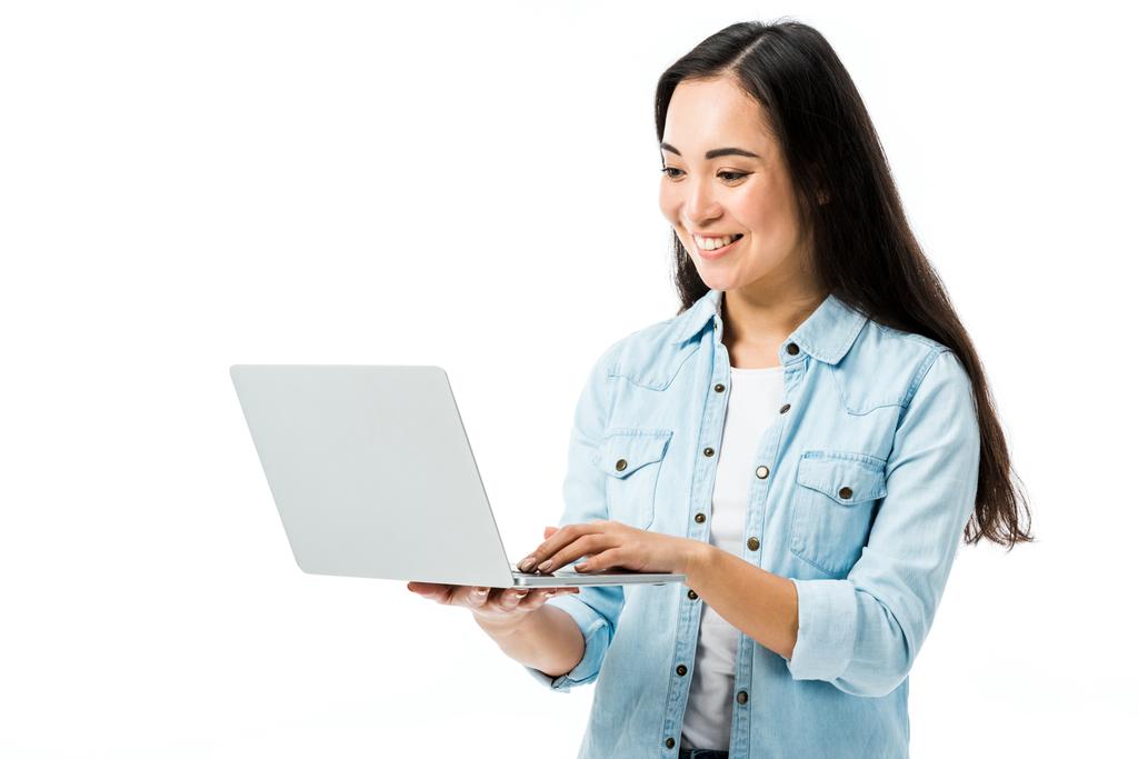 デニムシャツに身を包んだ魅力的なアジア系女性が笑顔でノートパソコンを持ち  - 写真・画像