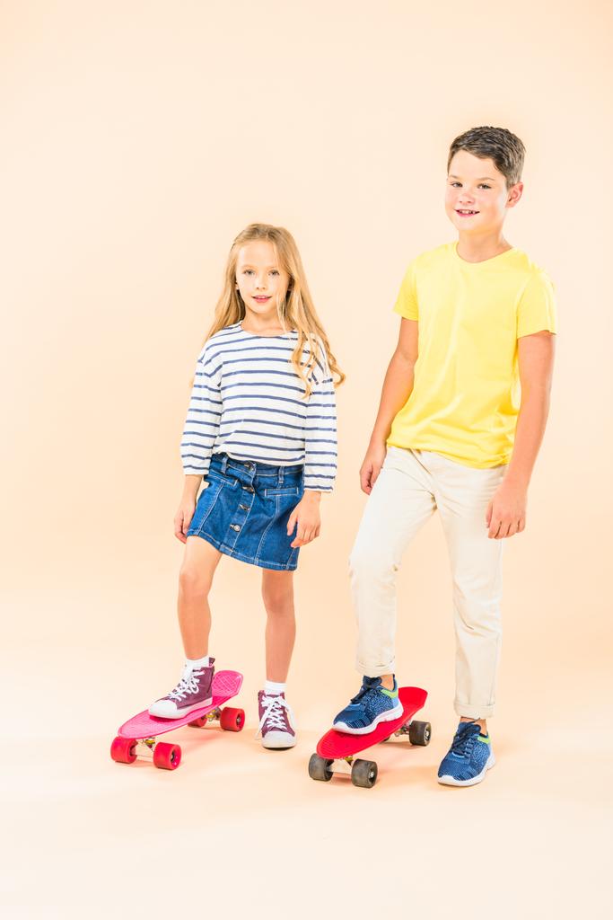 ピンクのスケートボードを持つ2人の笑顔の子供の完全な長さのビュー - 写真・画像