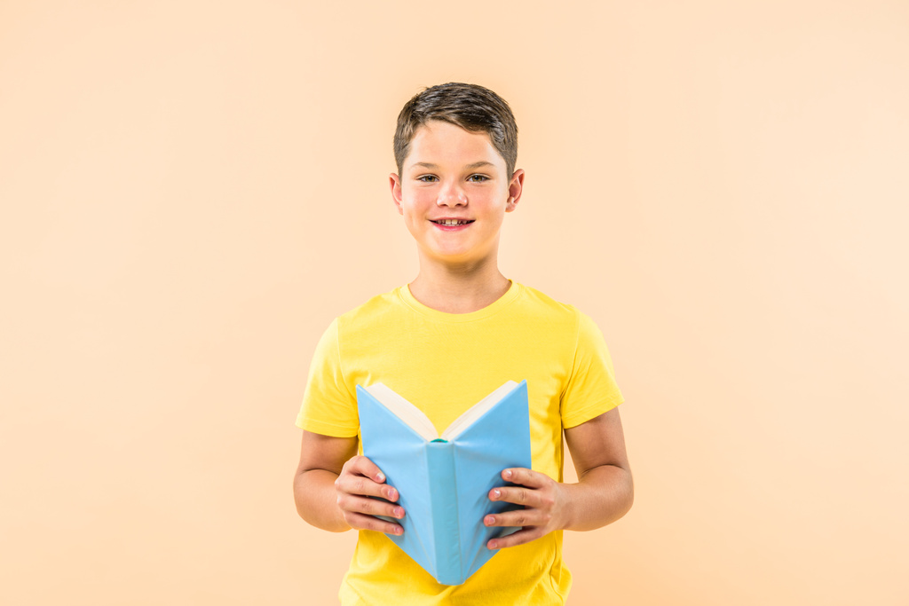vista frontal del niño en camiseta amarilla sosteniendo libro aislado en rosa
 - Foto, imagen