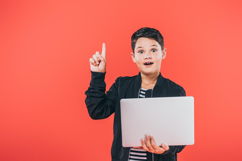Frontansicht eines staunenden Kindes in Jacke mit Laptop und Ideenschild isoliert auf Rot - Foto, Bild