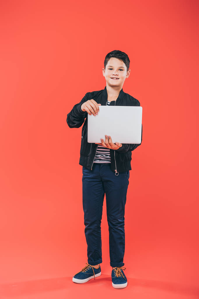 full length view of smiling kid using laptop on red - Photo, Image