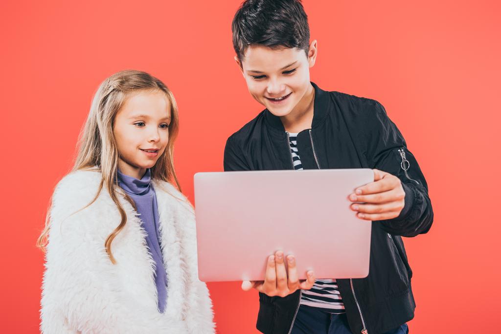 двое улыбающихся детей с ноутбуком, изолированным на красном
 - Фото, изображение