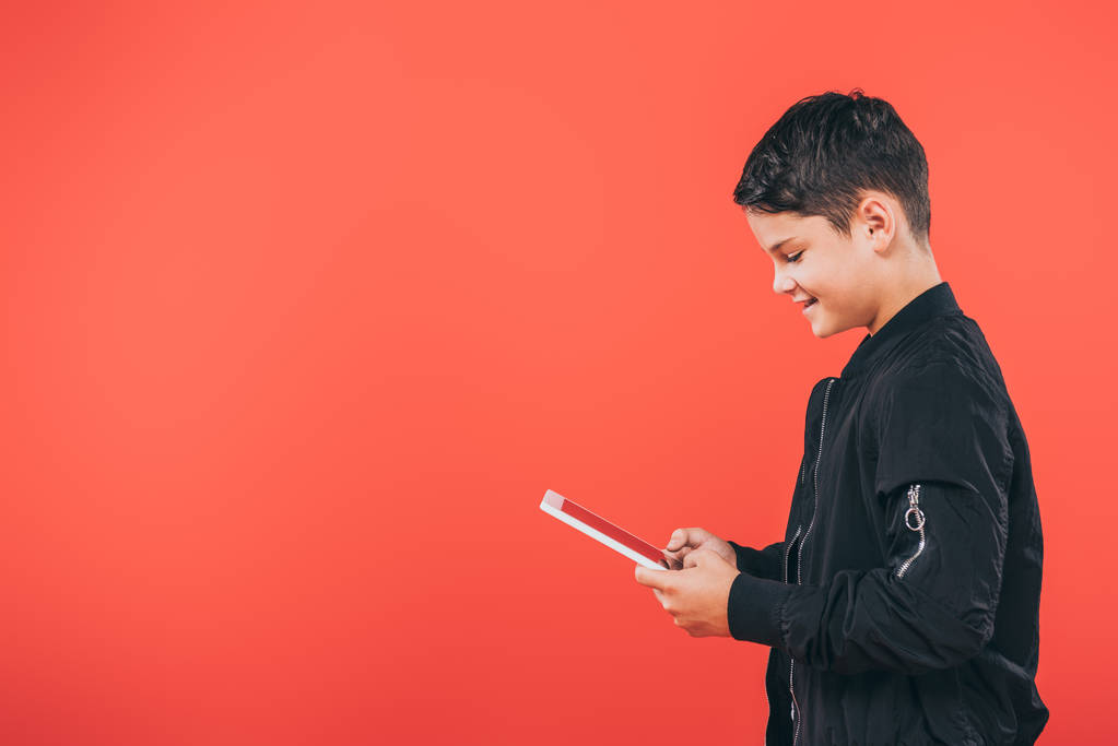 vista lateral del niño sonriente utilizando tableta digital aislada en rojo
 - Foto, imagen