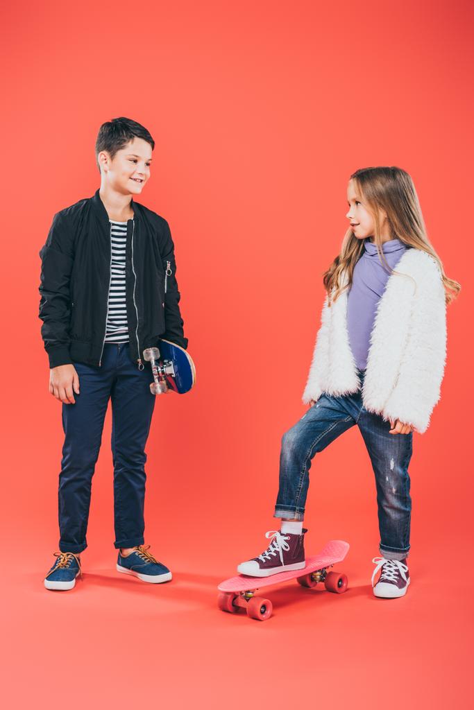 赤でお互いを見てスケートボードを持つ2人の子供の完全な長さのビュー - 写真・画像