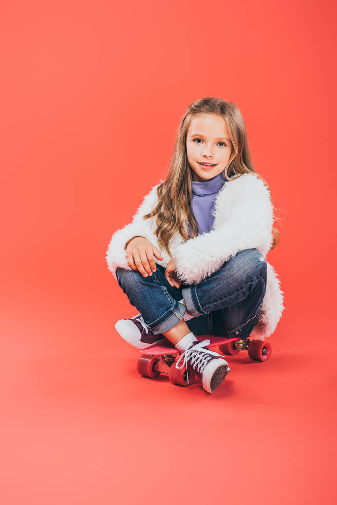 Lächelndes Kind im Herbst-Outfit auf Skateboard auf Rot - Foto, Bild