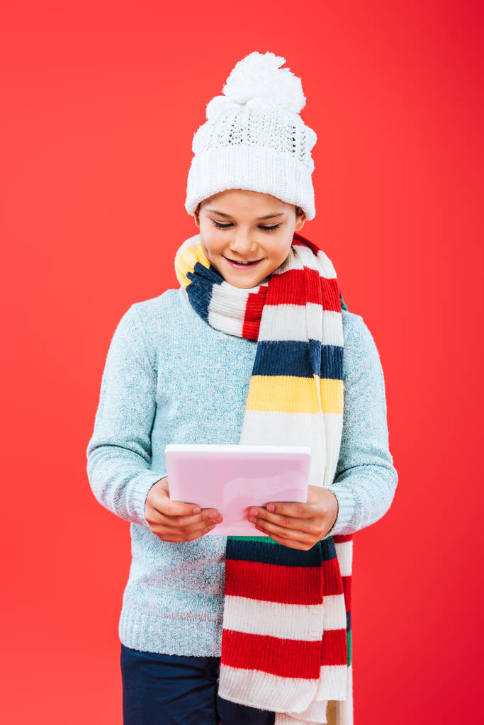 kırmızı izole dijital tablet kullanarak şapka ve eşarp gülümseyen çocuğun ön görünümü - Fotoğraf, Görsel