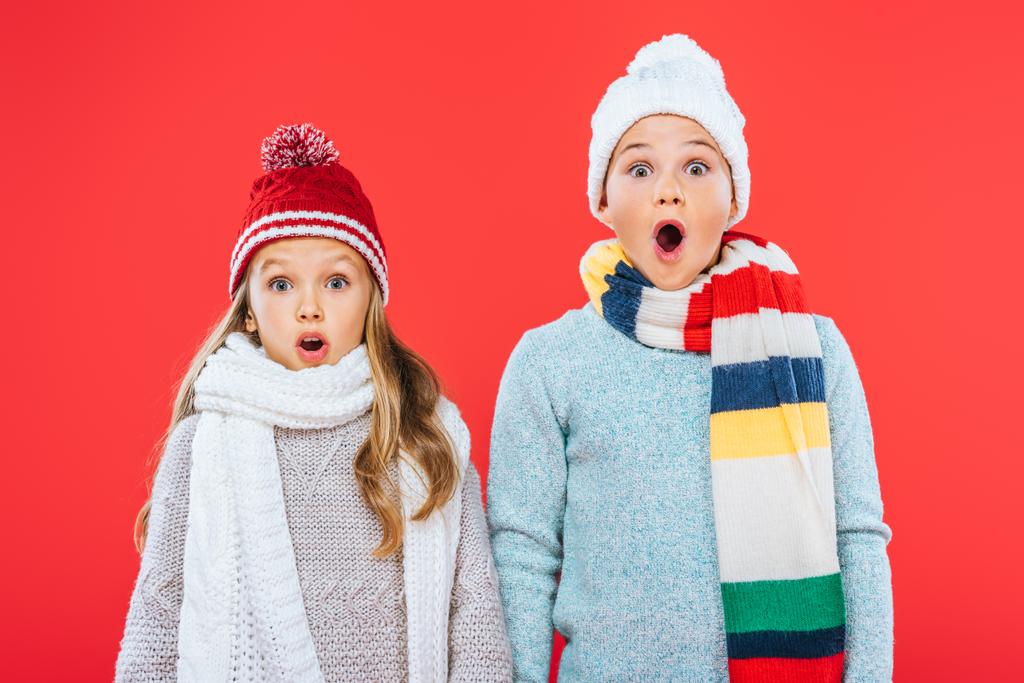 Vista frontal de duas crianças chocadas em roupas de inverno isoladas no vermelho
 - Foto, Imagem