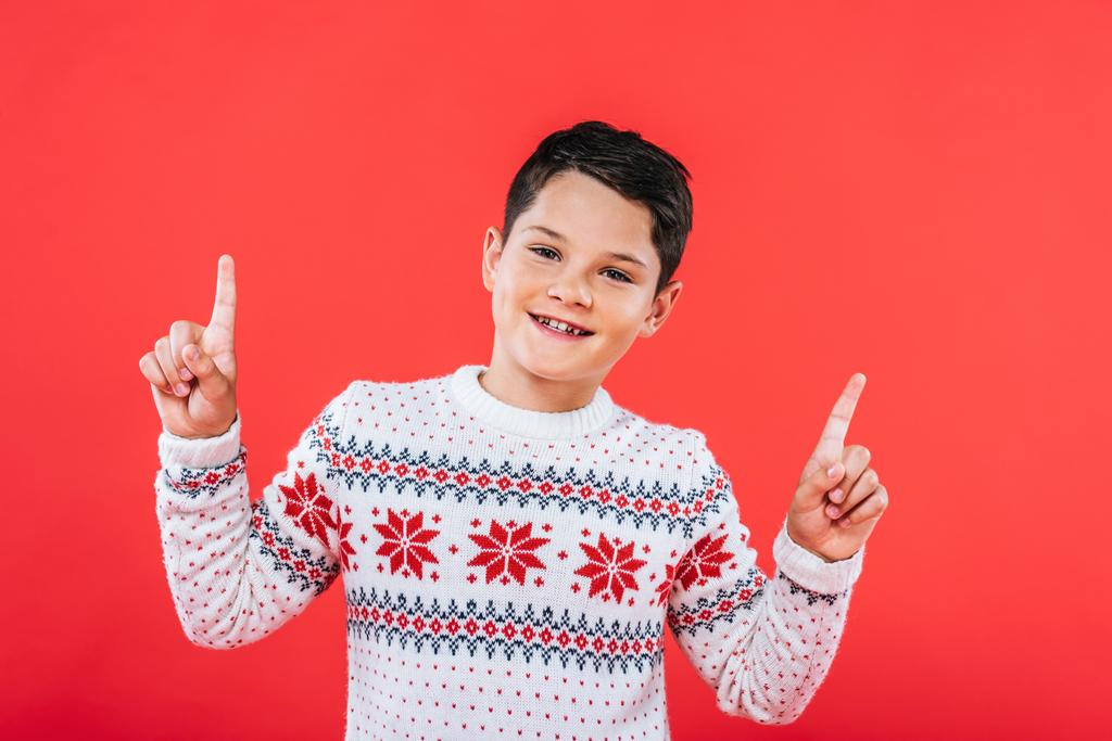 front view of smiling kid in sweater pointing with fingers isolated on red - Photo, Image