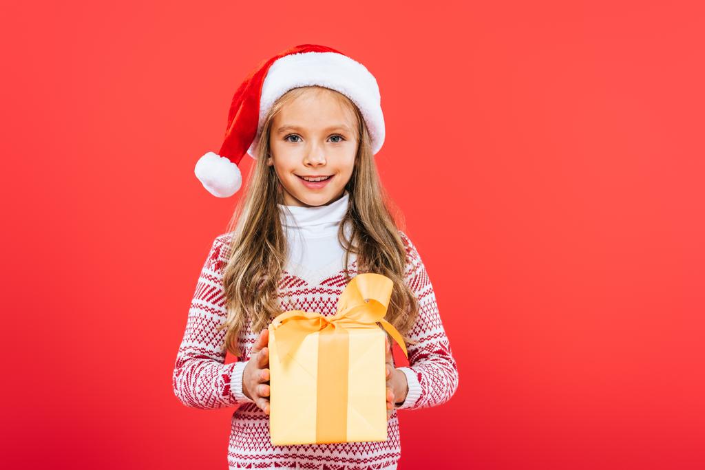 pohled na usmívající se dítě v Santa klobouku, současné izolované na červeném - Fotografie, Obrázek
