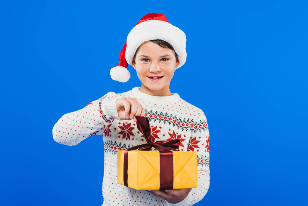 Widok z przodu dziecka w Santa kapelusz i sweter trzyma prezent na białym tle na niebiesko - Zdjęcie, obraz
