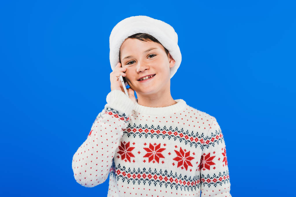 niño en suéter hablando en el teléfono inteligente aislado en azul
 - Foto, imagen