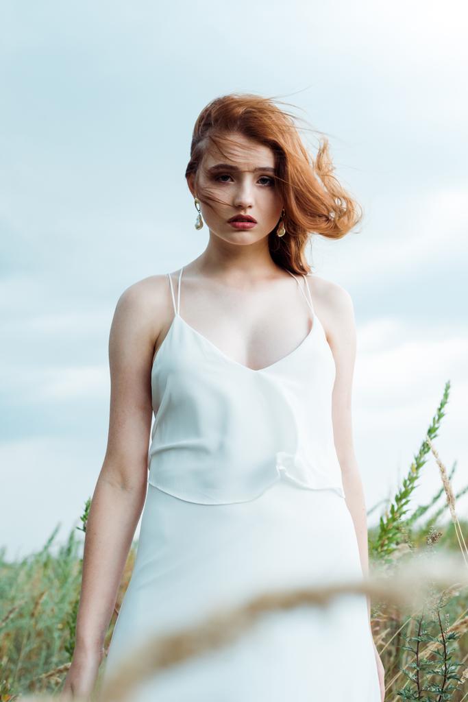 カメラを見て白いドレスを着た若い赤毛の女性の選択的な焦点  - 写真・画像