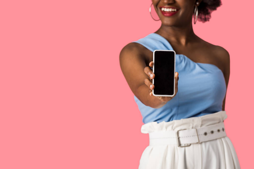 ピンクに隔離された空白の画面でスマートフォンを保持している陽気なアフリカ系アメリカ人の女の子のトリミングビュー  - 写真・画像