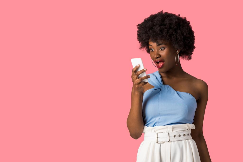 ピンクで孤立したスマートフォンを見てショックを受けたアフリカ系アメリカ人の女の子  - 写真・画像