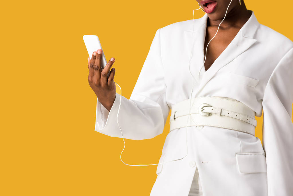 オレンジ色に隔離されたスマートフォンを持つ驚いたアフリカ系アメリカ人の女の子のトリミングビュー - 写真・画像