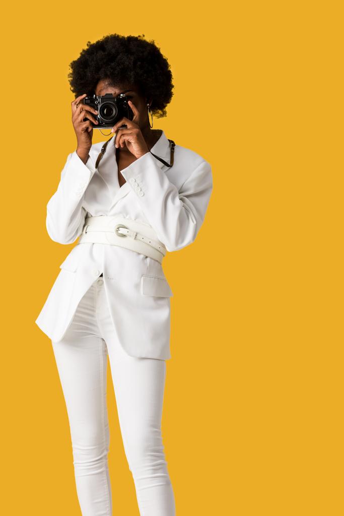 lockige afrikanisch-amerikanische Frau, die Gesicht bedeckt, während sie Fotos isoliert auf orange macht  - Foto, Bild
