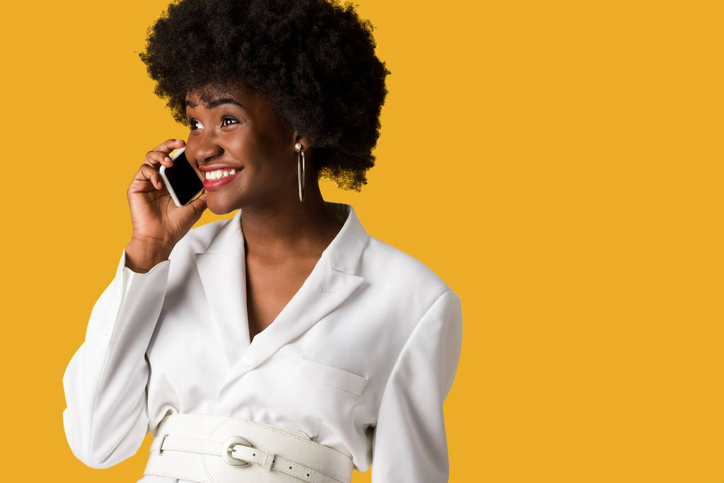 fröhliche und lockige Afroamerikanerin spricht auf Smartphone isoliert auf orange  - Foto, Bild