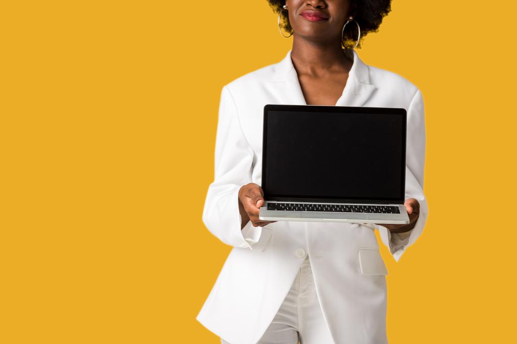 levágott kilátás boldog afro-amerikai lány gazdaság laptop üres képernyő elszigetelt narancssárga  - Fotó, kép