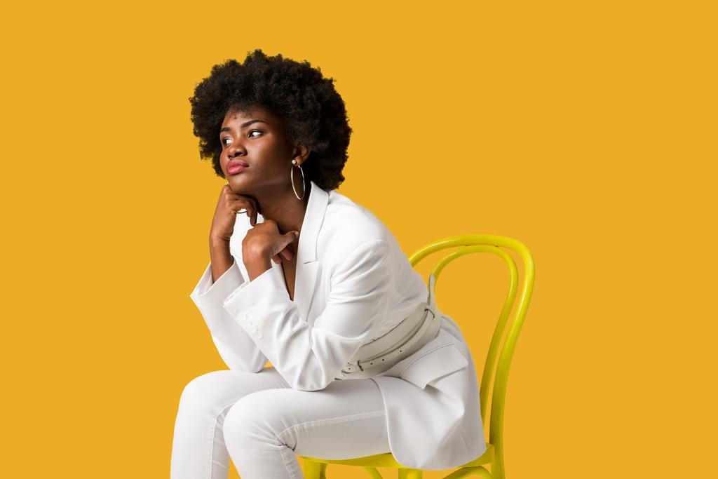 オレンジ色に孤立した黄色い椅子に座っている悲しいアフリカ系アメリカ人の女の子  - 写真・画像