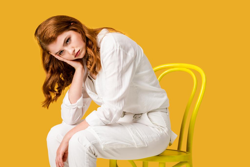 turuncu izole sarı sandalyede oturan üzgün kızıl saçlı kız  - Fotoğraf, Görsel