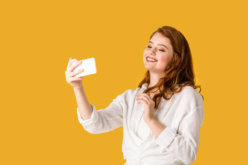 Szép Vöröshajú lány vesz selfie és mosolyogva izolált narancs  - Fotó, kép