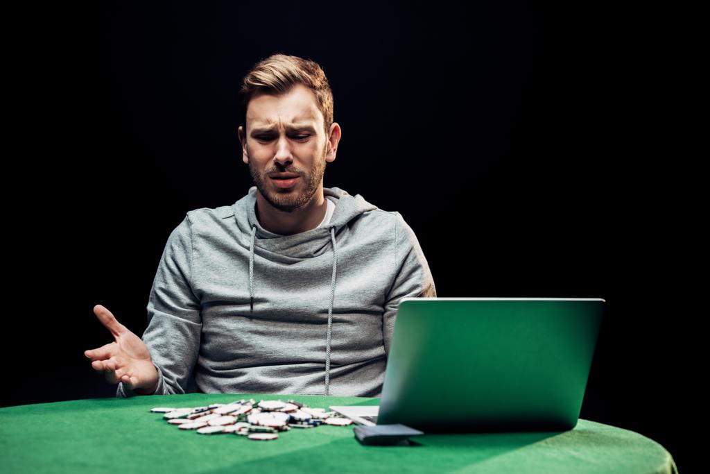 αναστατωμένος άνθρωπος την έκφραση κοντά σε φορητό υπολογιστή και μάρκες πόκερ απομονωθεί σε μαύρο  - Φωτογραφία, εικόνα