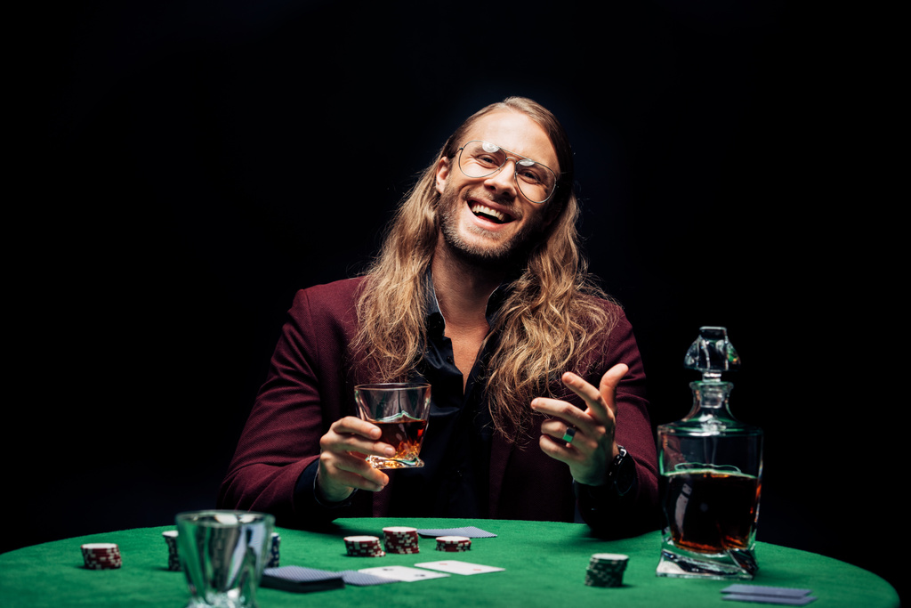 messa a fuoco selettiva di felice uomo barbuto in occhiali da vista in possesso di vetro con whisky vicino a carte da gioco isolate su nero
  - Foto, immagini