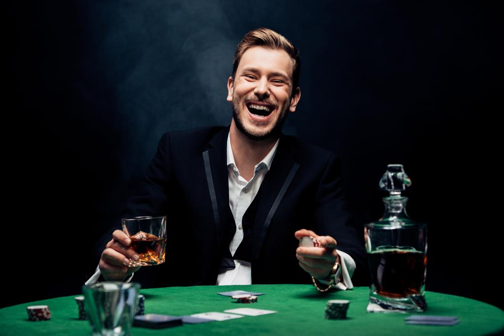 selective focus of cheerful man holding glass with alcohol on black with smoke  - Photo, Image