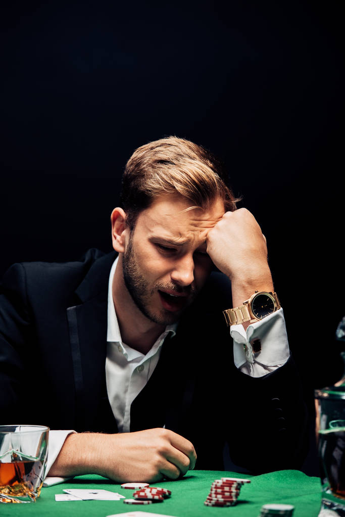 επιλεκτική εστίαση της αναστατωμένος άνθρωπος κοντά στο τραπέζι με μάρκες πόκερ που απομονώνονται σε μαύρο  - Φωτογραφία, εικόνα