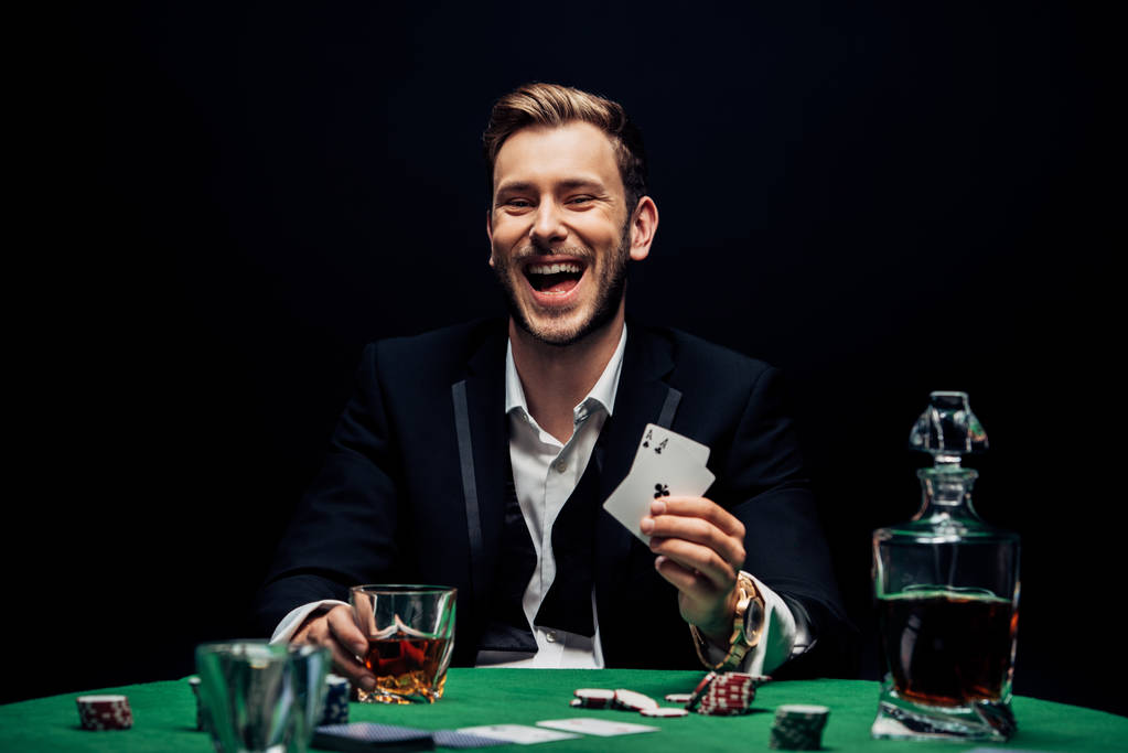 QUIIV, UCRÂNIA - 20 DE AGOSTO DE 2019: foco seletivo do homem alegre segurando vidro com álcool e jogando cartas isoladas em preto
  - Foto, Imagem
