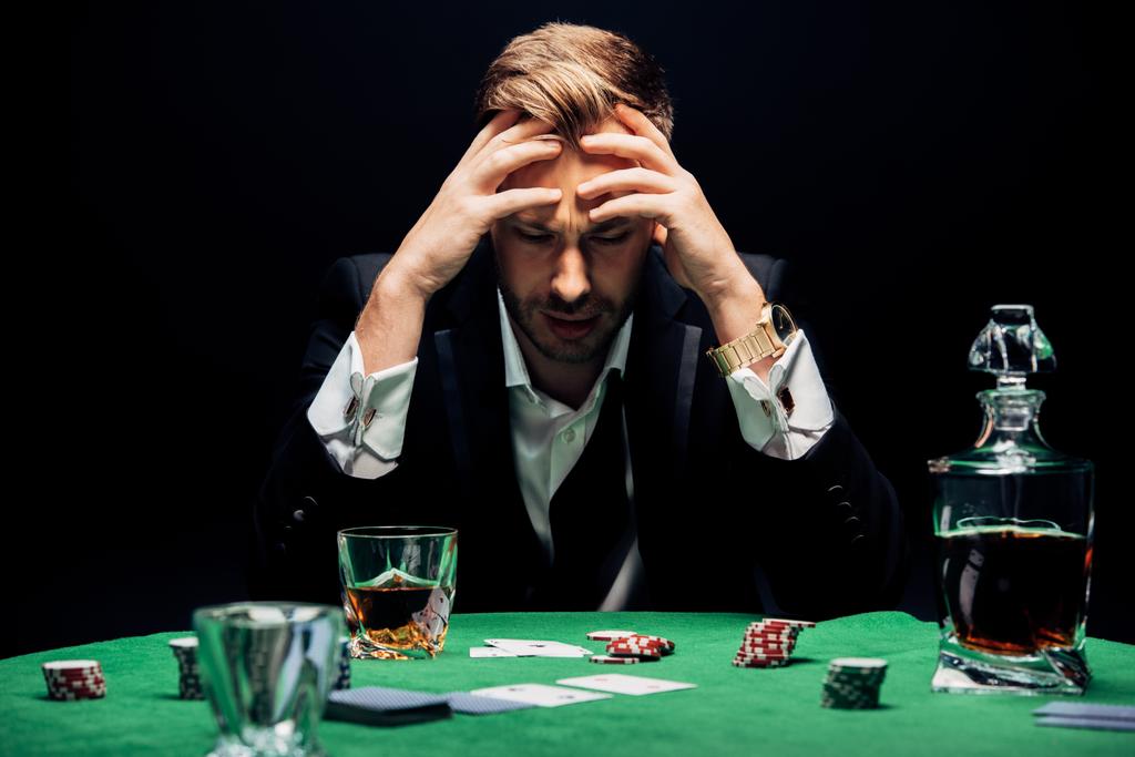 selective focus of sad man sitting near poker table isolated on black  - Photo, Image